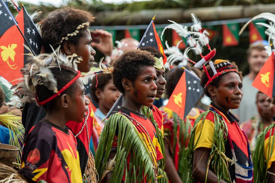 Children in traditional Papua New Guinean dress holding PNG flags at a celebration
